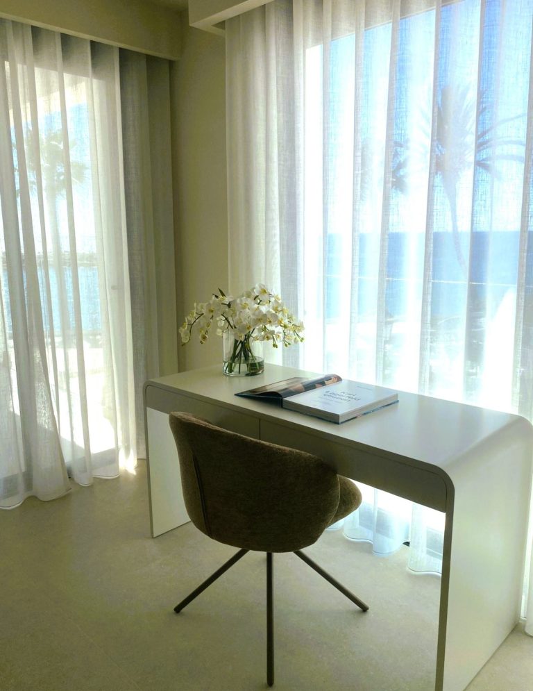 INTERIORISMO FUENGIROLA Salón moderno con sillas de madera, mesa de centro y estantería, con luz natural abundante.