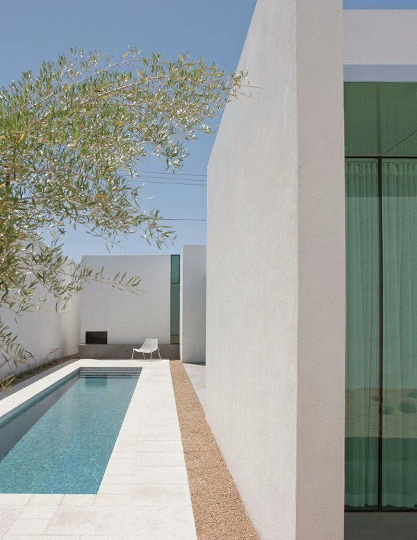 Salón moderno con sillas de madera, mesa de centro y estantería, con luz natural abundante.