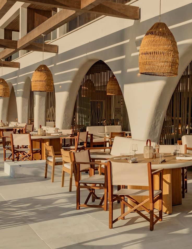 INTERIORISMO FUENGIROLA Salón moderno con sillas de madera, mesa de centro y estantería, con luz natural abundante.